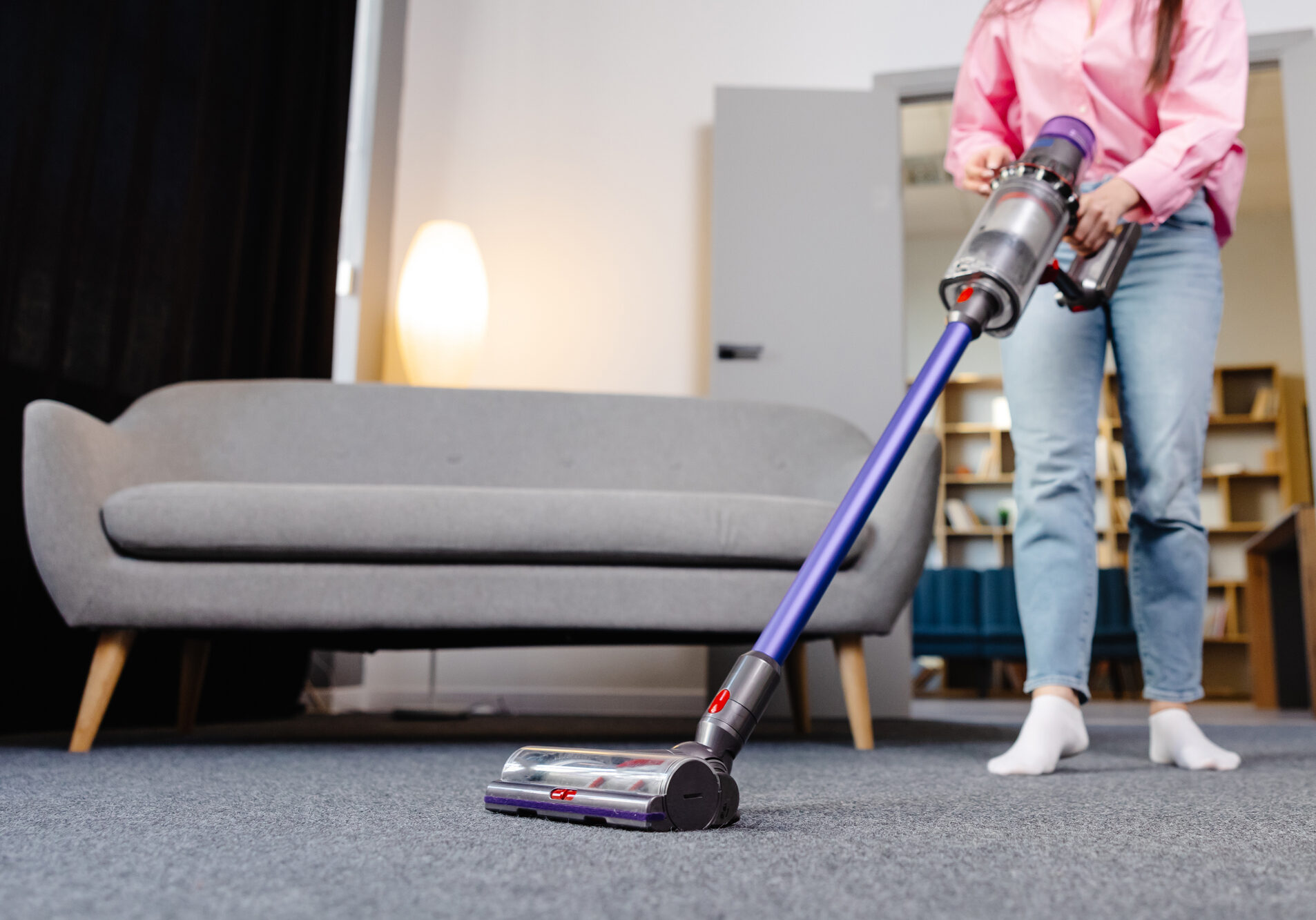 Young woman uses cordless vacuum cleaner to clean home carpet. Modern easy cleaning.